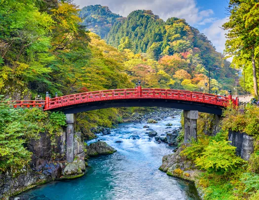 Red bridge over an active river, with large mountains in the background