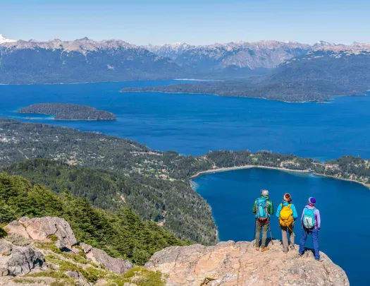 Group of 3 people standing on a cliff, looking out to a lake