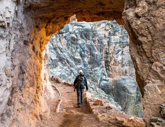Archway shot of guest hiking down trail, towards rock face.