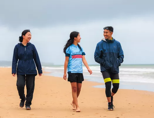 Two women and one man smiling while walking on a beach