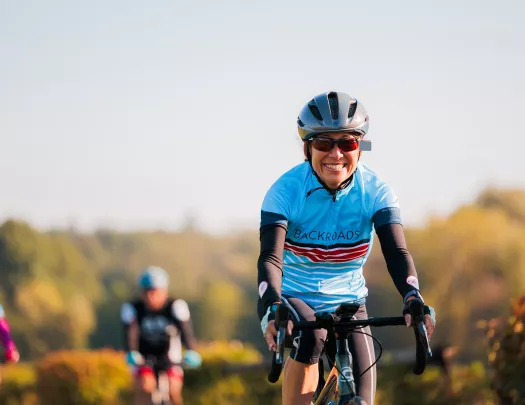 Woman smiling while riding a bike, wearing a helmet and sunglasses