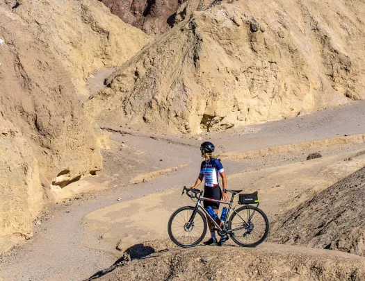 Woman standing next to her bike on a boulder, looking out to large canyons