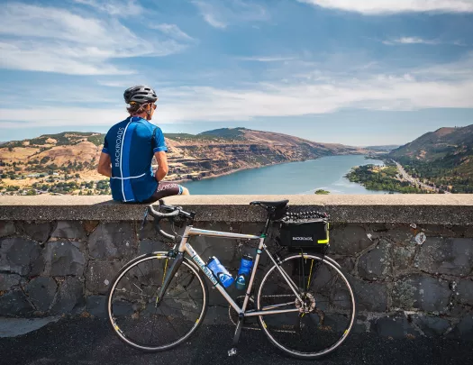 Man sitting on a stone ledge looking out to a lake, with a bike leaning on the ledge