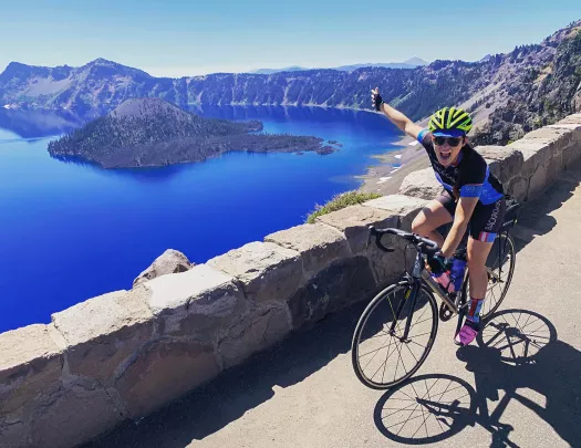 Guest cycling and gesturing towards Crater Lake on her right.