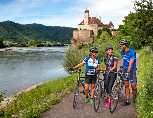 Three bikers walking their bikes on a path along the Danube River.