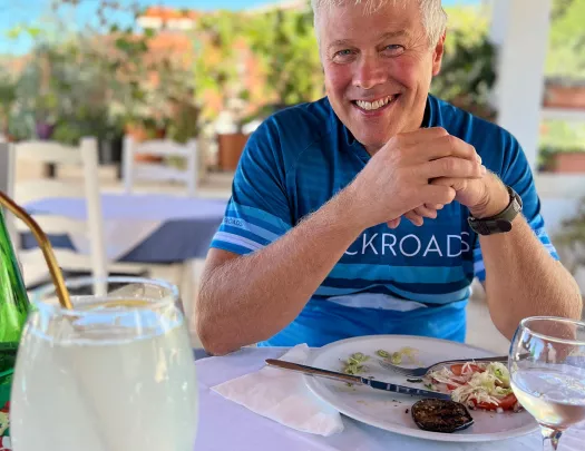 Guest in bike gear at meal, smiling at camera.