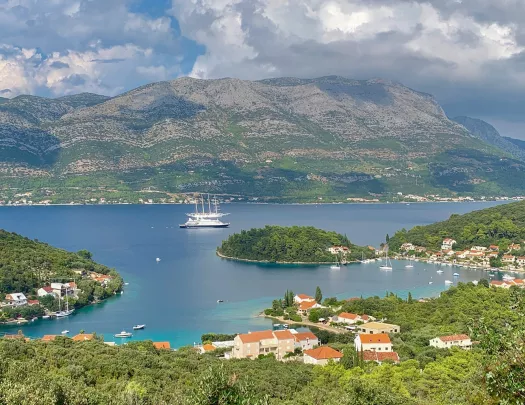 Wide shot of coastal Croatian town, mountains, large river, boat behind.