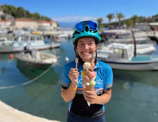 Guest/leader in front of boats, large ice cream in hand.