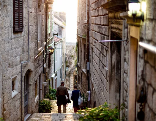 Two people walking down narrow alleyway during sunset.