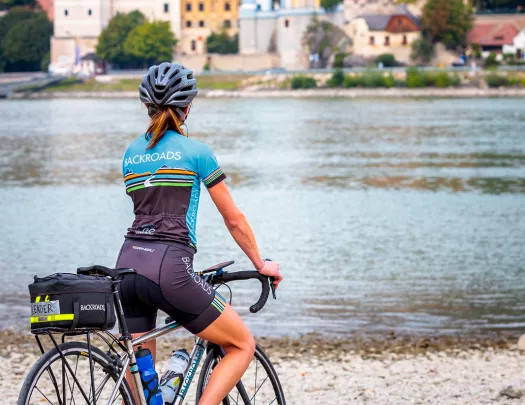 Biker at the edge of the water, looking across at a church tower.