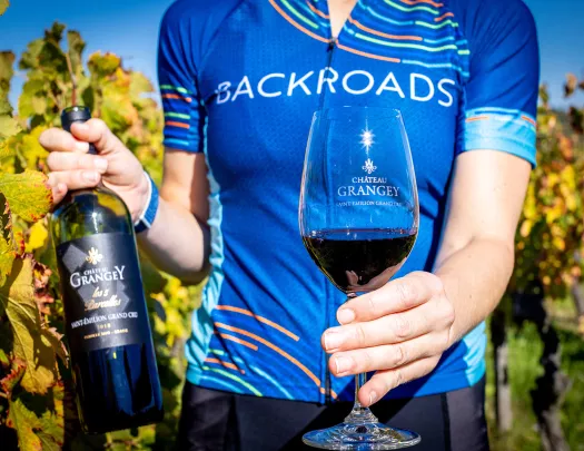 Leader in jersey with red wine bottle, glass, vineyard behind them.