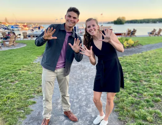 Two guests waving and posing for camera, lake and boats in bakcground.