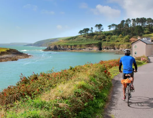 Man in a blue jersey, riding a bike on a road along a large lake