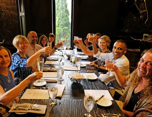 Group of guests at wooden dinner table. Toasting glasses.