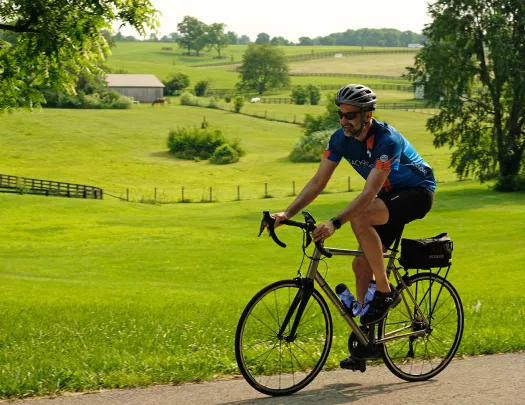 Guest cycling past farmhouses, grassy meadow.
