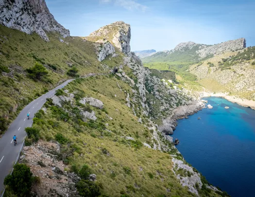 Two bikers riding around a bend on the coast of Mallorca.