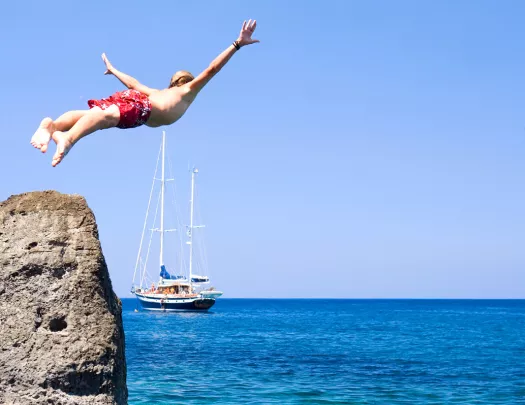 Swimmer diving off of a cliff into crystal clear waters.
