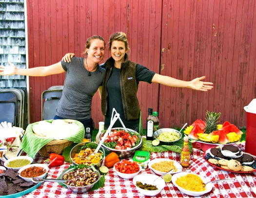 Two people posing behind lunch spread.