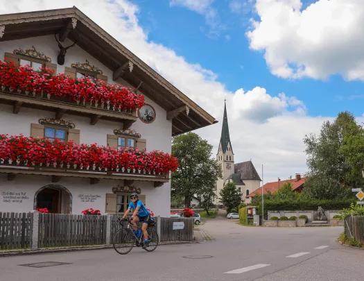 Biker riding past house with large pink and red floral displays on balconies.