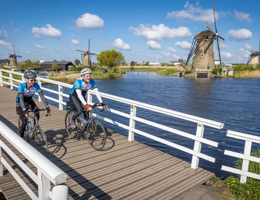 Bikers on small bridge with windmills in background