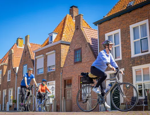 Three guests cycling past brick housefronts.