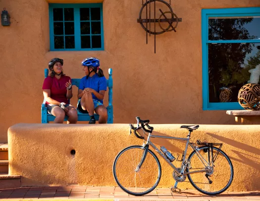Two women sitting in front of an orange house, with a bike parked out front