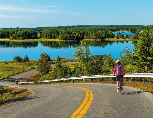 Guest cycling down road, large lake or river in background.