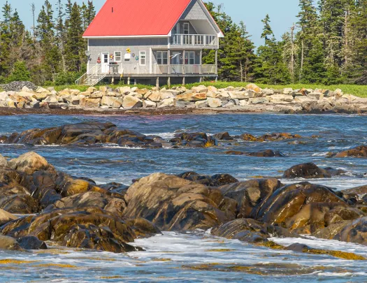 Rocky ocean shore in foreground, two-story fishing house in background.