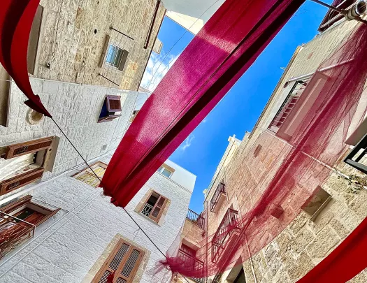 Point of view shot of sky, tops of white houses and red tapestries flowing between them.