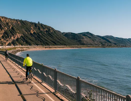 People biking along coastal road, ocean beside them.