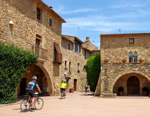 Two guests cycling through village, tan stone buildings all around.