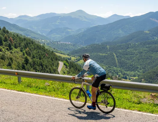 Man riding a bike on a road, with large valleys of trees in the distance with large hills