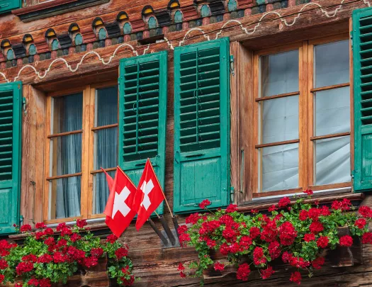 Wooden cabin building, with three Swiss flags and flower beds under a window