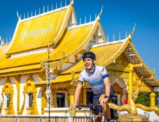 Man smiling while biking in front of a white and gold temple