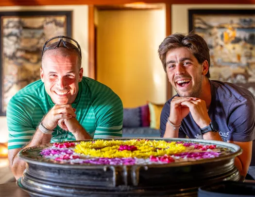Two men smiling with standing in front of a small fountain full of flowers