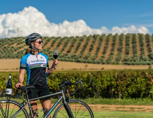 Backroads guest holding a glass of wine with a vineyard in the background.