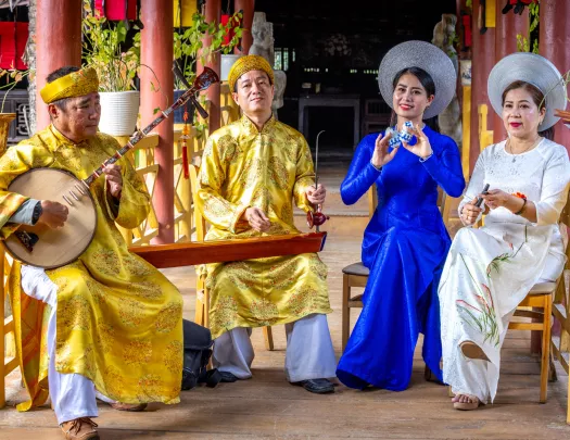 Two men and two women wearing traditional Vietnamese attire while playing instruments