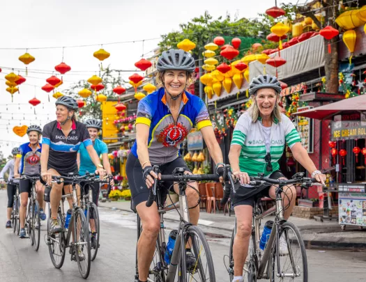Group of women riding bikes on a road with markets to the right