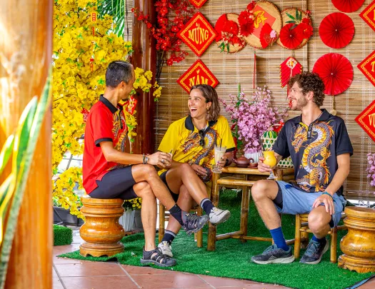 Two men and one woman sitting on wooden chairs in front of Vietnamese art pieces