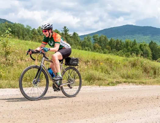 Woman riding a bike on a dirt road, with a grassy hill in the background