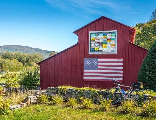 Shot of bike in front of red barn, US flag on barn wall.