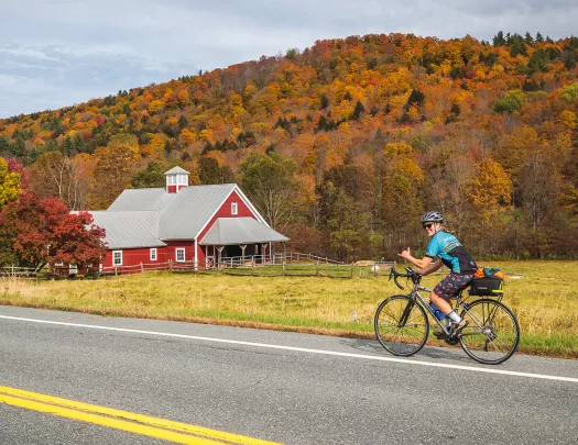 Guest cycling past red farmhouse. Fall trees behind.