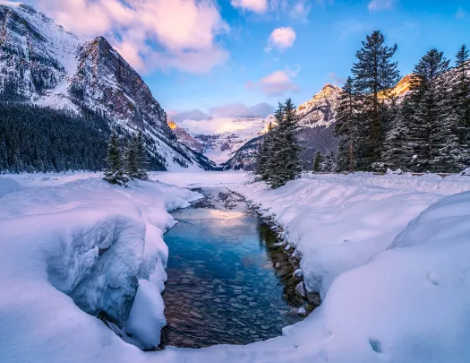 Wide shot of snowy valley, mountains, trees around.