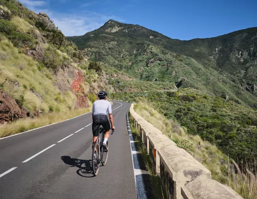 Person riding their bike on a road with large, grassy mountains in the distance