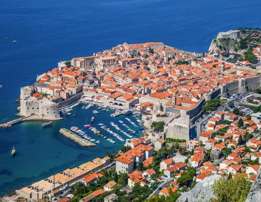Bird's eye shot of Dubrovnik coastline, walled city, small boats, etc.