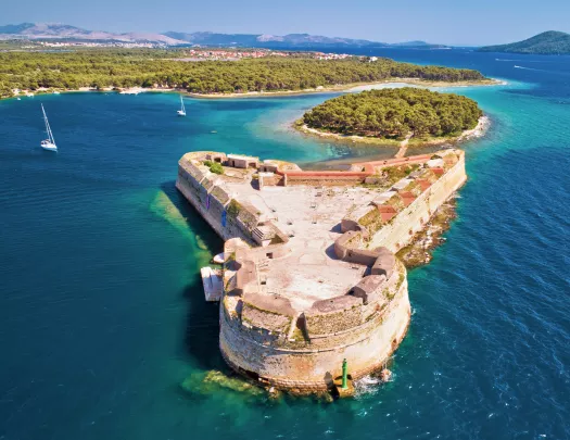 Stone, rustic building in the ocean, with a forest in the background