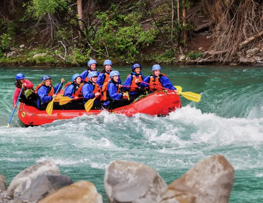 Group of men and women in a red raft paddling through a river