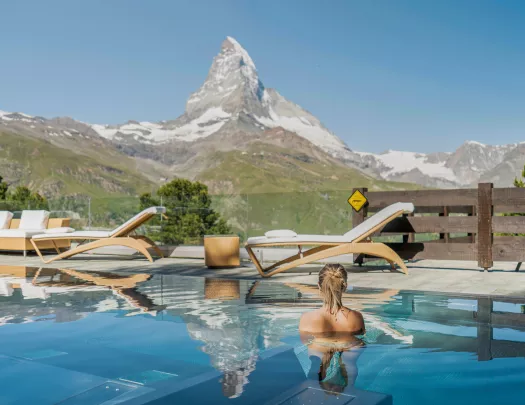 Woman swimming in an outdoor pool looking out towards a tall mountain