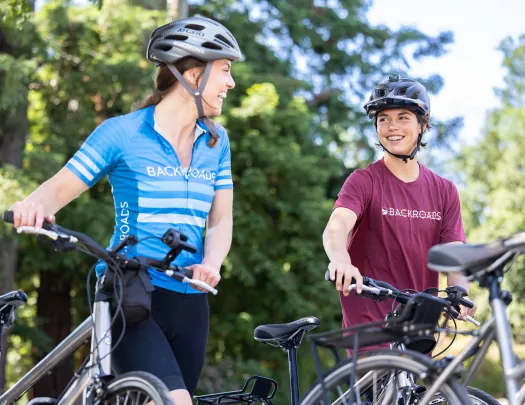 Two guests walking with their bikes, talking, both smiling.