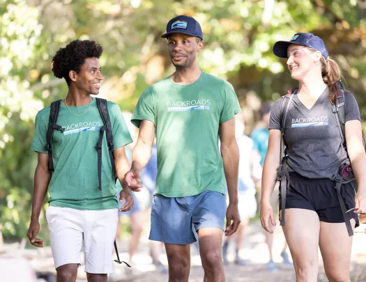 Two men and one woman walking on a trail with blurry trees in the background